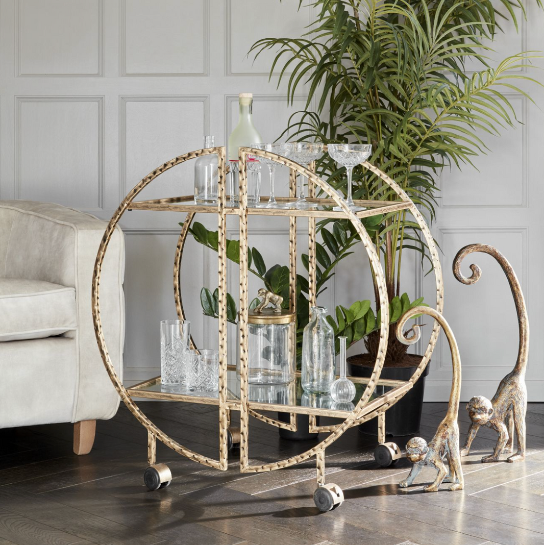 Antique gold drinks trolley with mirrored shelves, styled with bottles and cocktail glassware.
