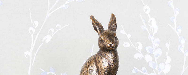 A decorative animal ornament of a rabbit in antiqued gold in front of a gray wall