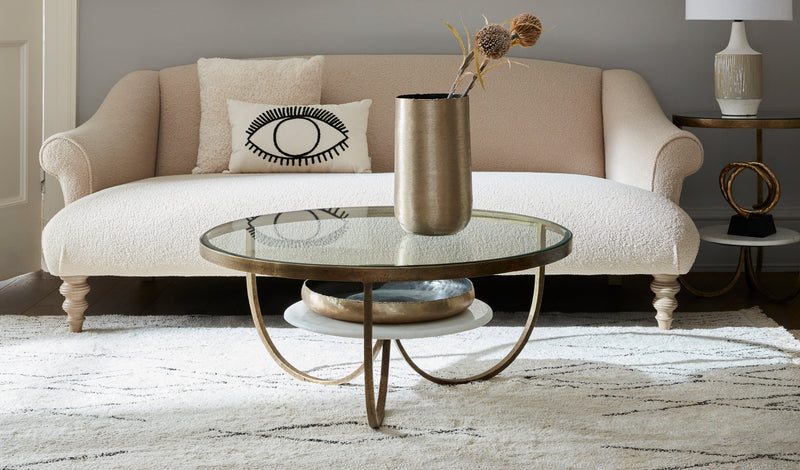 A round glass coffee table in a neutral living room