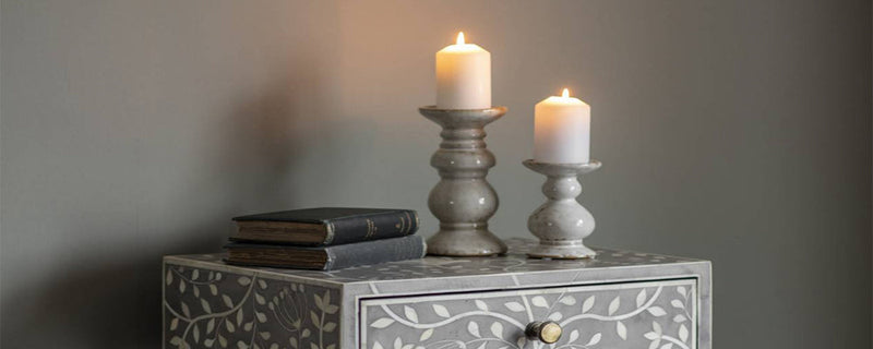 A pair of candles sit on grey holders on top of a chest of drawers