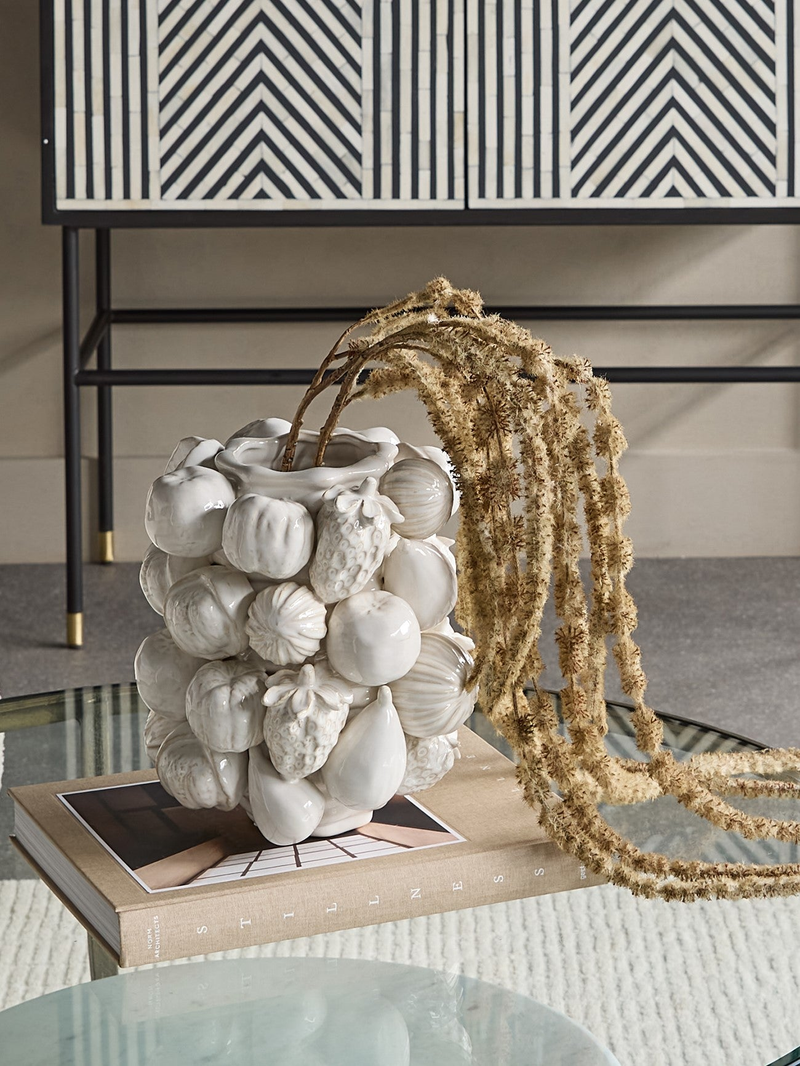 A decorative shell vase, with faux plant on a coffee table.