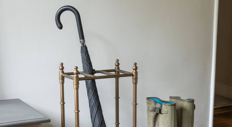 An umbrella in a rack next to some boots, in a hallway