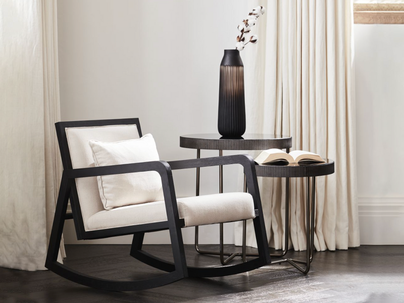 A rocking chair in black wood with white cushions next to a next of tables within our unique furniture collection