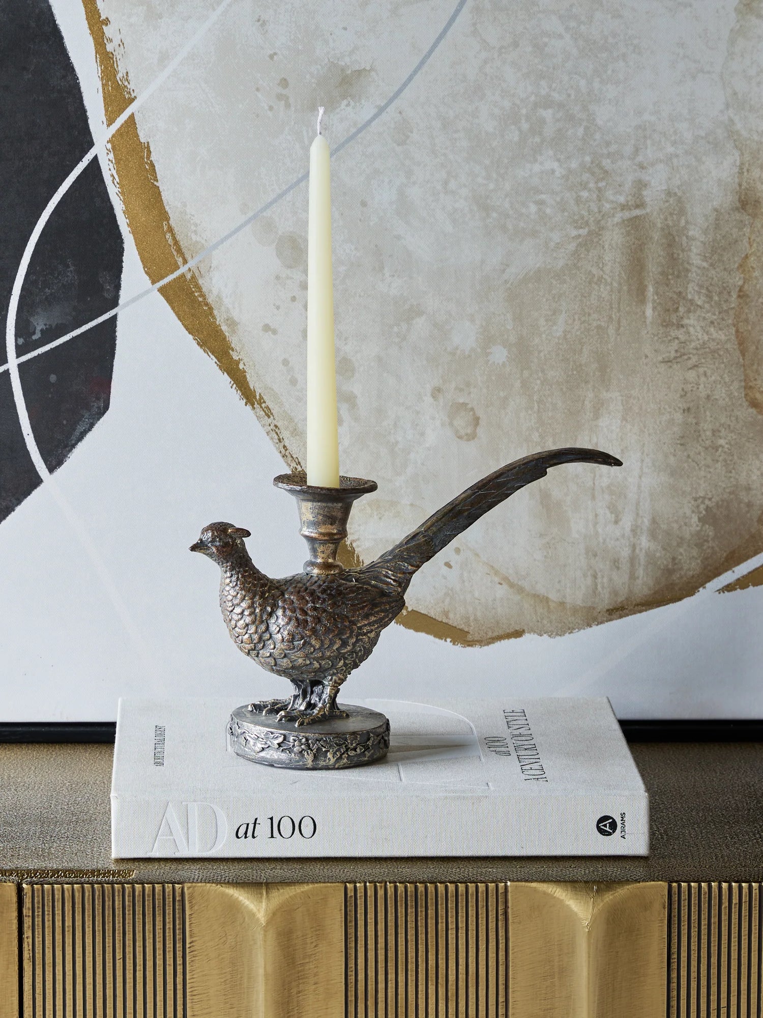 A Decorative pheasant bird candle holder on a book with a textured wall in the background