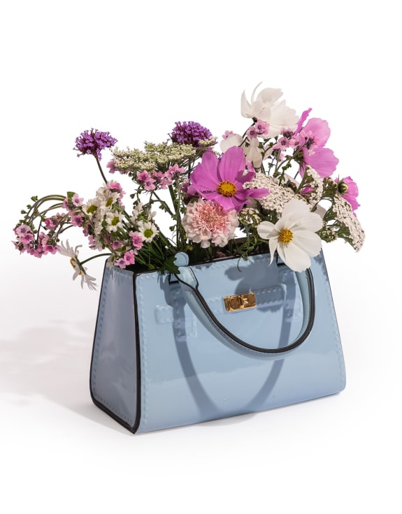 Handbag vase in light blue, made from ceramic filled with flowers on a white background