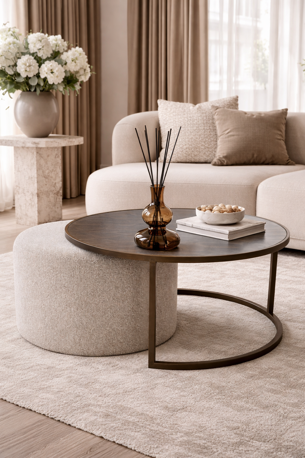 A brown glass reed diffuser on a round coffee table, ottoman, and sofa with decorative pillows.
