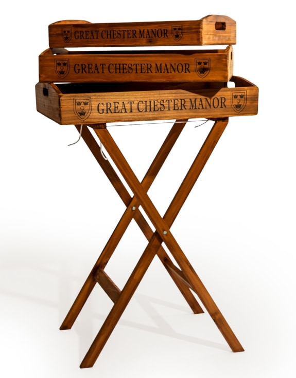 Three stacked wooden serving trays engraved with 'GREAT CHESTER MANOR' and crest emblems, displayed on a folding wooden stand 