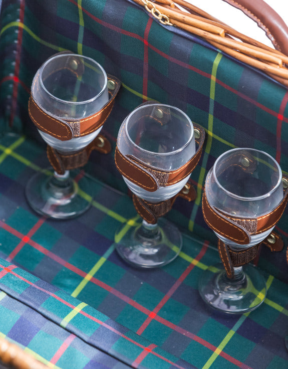 Three wine glasses secured with brown leather straps in a picnic hamper with tartan lining